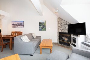 Ein Wohnzimmer mit Kamin, Fernseher, einer Couch, einem Holztisch und einer Essecke mit Stühlen und Tisch.