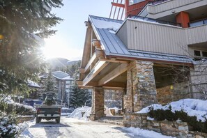Un immeuble à plusieurs étages, doté d’une façade en pierre, d’une entrée couverte et d’un véhicule garé devant.
