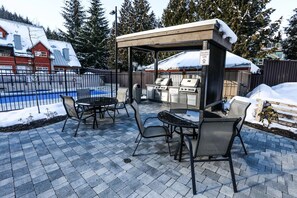 Une terrasse extérieure avec un espace barbecue, une piscine et un coin salon abrité.