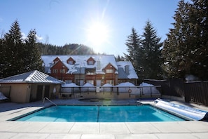 Une piscine avec un toboggan, une terrasse couverte et un bâtiment dont le toit est recouvert de neige.