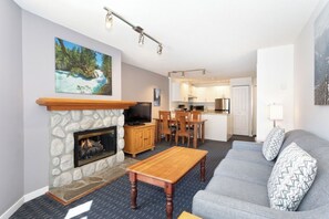 Ein Wohnzimmer mit Kamin aus Stein, einem Fernseher, einem Essbereich und einer Küche im Hintergrund.