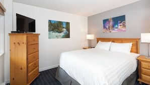 A hotel room with a bed, a wooden dresser, a flat-screen TV, two wall-mounted paintings, and a nightstand with a lamp. - Creekside Haven | Heated Pool, Fireplace & Easy Ski Access | Close to Gondola (Whistler)