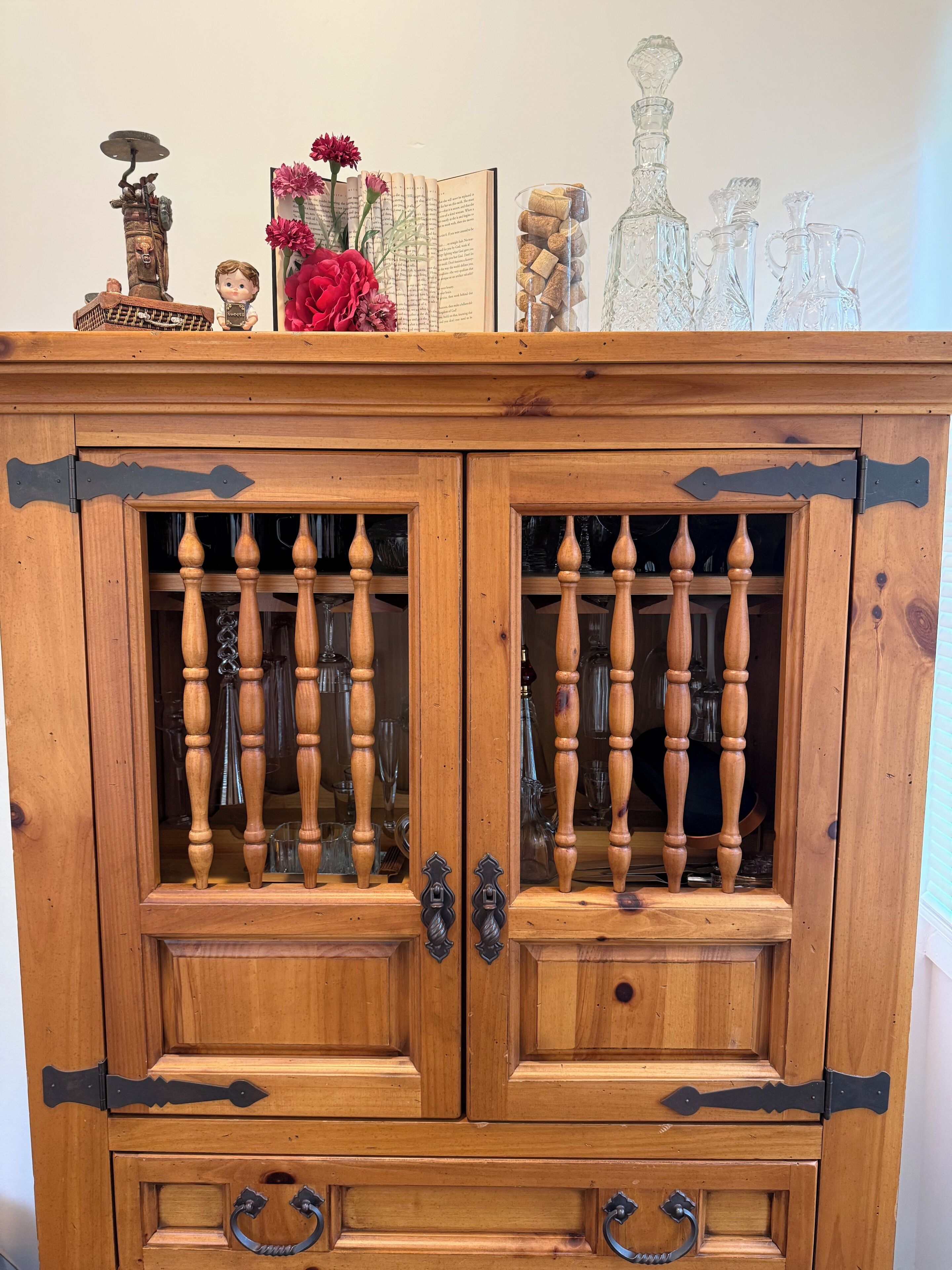 Un meuble en bois doté de portes en verre, agrémenté de poignées décoratives et d’une petite étagère sur laquelle sont posés divers objets.