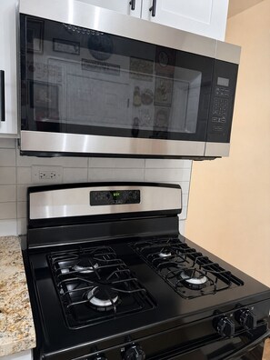A kitchen with a stainless steel microwave, a digital clock, and a gas stove with four burners.
