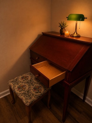 A wooden desk with a green lamp, a small potted plant, and a candle on the side.