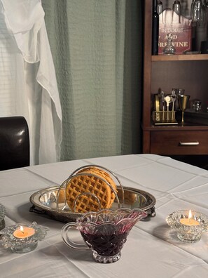 A table with a waffle, a glass pitcher, and two candle holders.