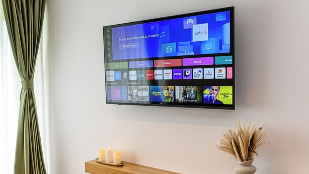 Et fladskærms-tv monteret på en væg, der viser en brugerflade med forskellige app-ikoner og en besked på et fremmedsprog.