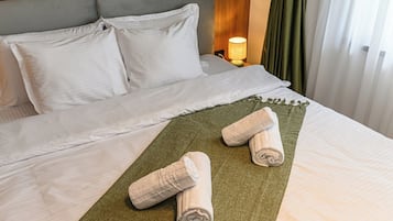 Ein Hotelzimmer mit einem Bett, Kissen, einer grünen Tagesdecke und zwei gerollten Handtüchern.