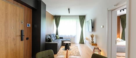 A modern living room with a sofa, a dining table, and a TV mounted on the wall.