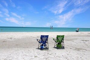 Ein Strand mit zwei Liegestühlen, einem entfernten Boot und einer Person im Wasser.