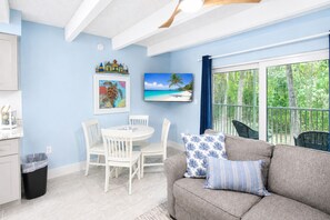 A room with a dining table, chairs, a sofa with patterned cushions, a framed picture, and a window with a view of greenery. - Sanibel Island - Walk to Beach Colony Inn 10 (Sanibel)