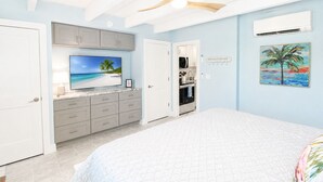 Ein Schlafzimmer mit Bett, Fernseher, Küchenzeile und einer Tür zu einem weiteren Raum.