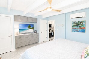 Ein Schlafzimmer mit Bett, Fernseher, Küchenzeile und einer Tür zu einem weiteren Raum.