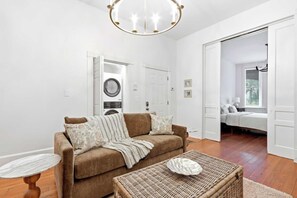 A living room with a brown sofa, a round coffee table, a wicker ottoman, and a ceiling light fixture. - The Oglethorpe Retreat of 1872 | Walk Everywhere (Savannah)