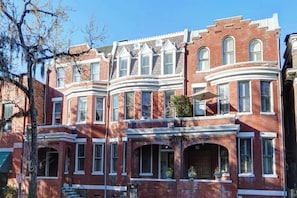 A row of red brick townhouses with white trim, large windows, and a bay window on the second floor. - The Oglethorpe Retreat of 1872 | Walk Everywhere (Savannah)