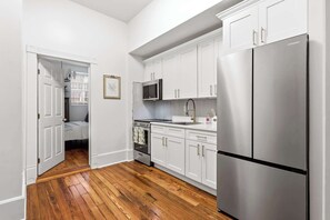 A compact kitchen with white cabinetry, stainless steel appliances, and a wooden floor. - The Oglethorpe Retreat of 1872 | Walk Everywhere (Savannah)