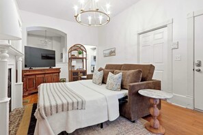 A room with a bed, a brown sofa, a small round table, a television, and a decorative mirror. - The Oglethorpe Retreat of 1872 | Walk Everywhere (Savannah)