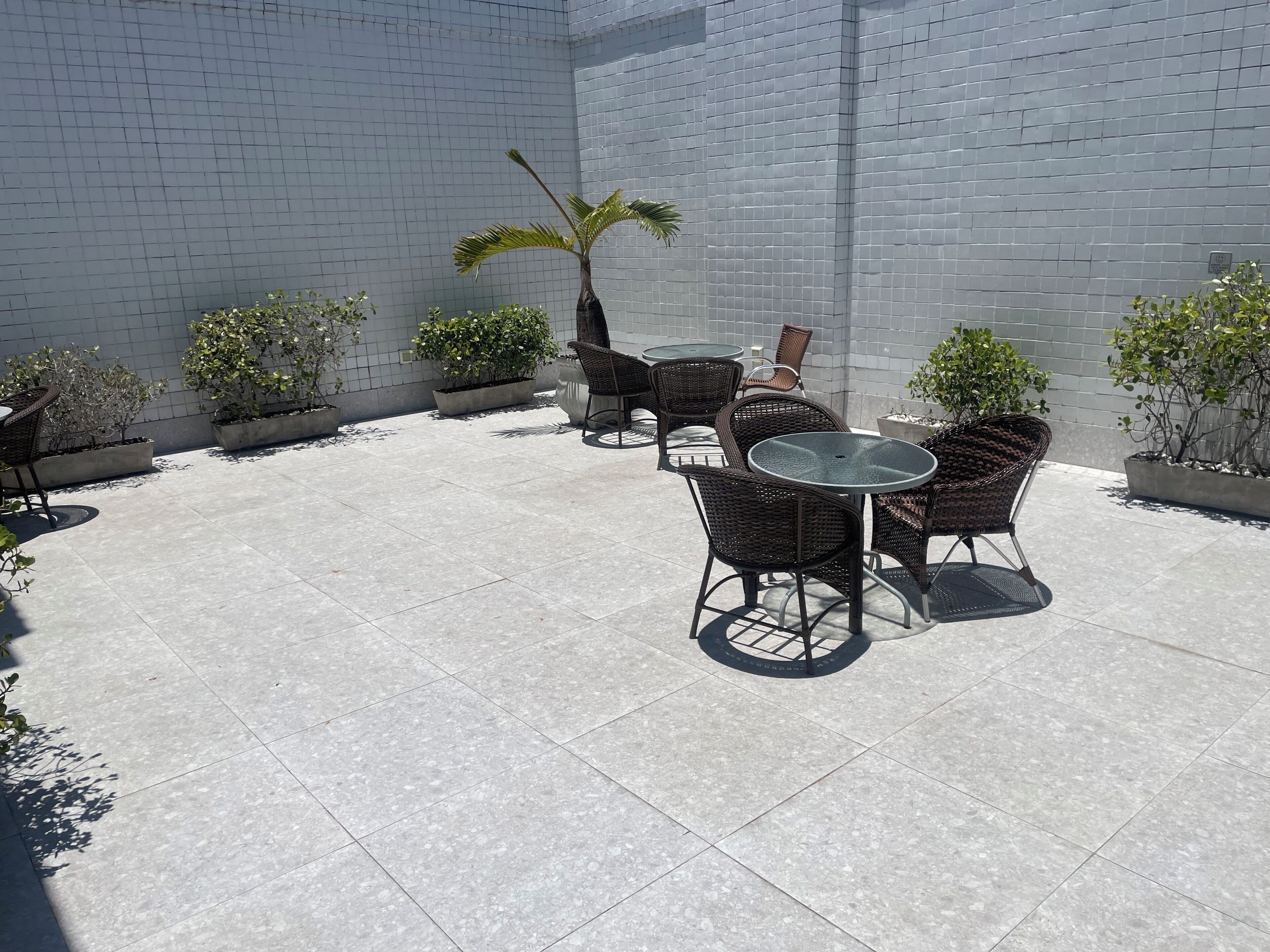 An outdoor patio with tiled flooring, wicker furniture, and potted plants.