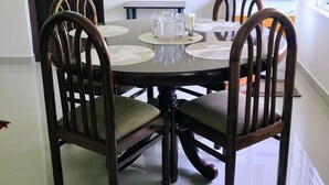 A dining area with a round table, four wooden chairs with cushioned seats, and a set of clear glassware on the table.