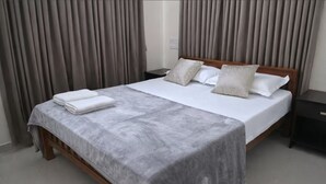 A hotel room with a bed, curtains, a nightstand, and a bedside table.