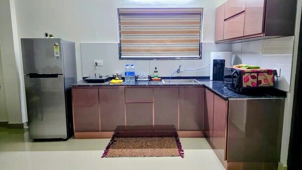A compact kitchen with a refrigerator, a microwave, a sink, and a window with blinds.