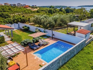 A swimming pool with lounge chairs and a covered seating area, surrounded by a white wall and greenery. - Villa Demian by Interhome (Pula/Banjole)