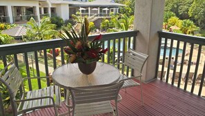 A balcony with a round table and two chairs, overlooking a pool and lush greenery. - North Shore living 2-bedroom condo in delightful Princeville's Wyndham Bali Hai (Princeville)