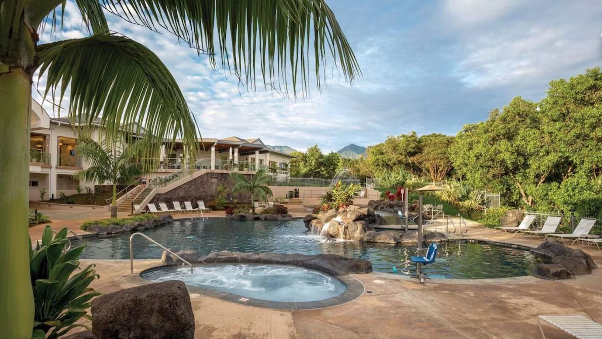 A resort pool area with a hot tub, lounge chairs, and a staircase leading to a building.