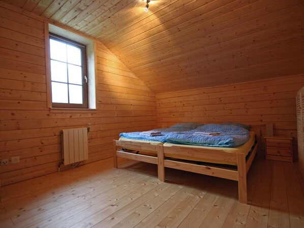 A small, single-room cabin with a wooden interior, a window, a bed, and a radiator.