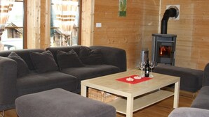 A cozy room with a sofa, ottoman, and a table with a bottle and glasses. A fireplace is visible in the background. - Baum-Hüsli, (Grächen). 8-Bettwohnung by Interhome (Grächen)