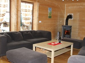 A cozy room with a sofa, ottoman, and a table with a bottle and glasses. A fireplace is visible in the background. - Baum-Hüsli, (Grächen). 8-Bettwohnung by Interhome (Grächen)