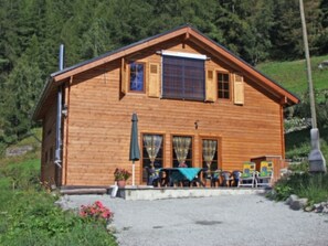 A wooden cabin with a porch, a table, and chairs.