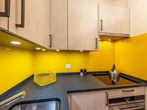 A kitchen with wooden cabinets, a stainless steel kettle, and a yellow wall. - Ambassador "Yellow Home", (Grächen), 1048 by Interhome (Grächen)