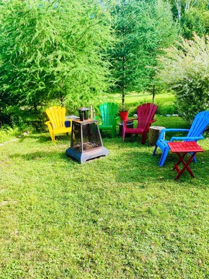 An outdoor seating area with colorful Adirondack chairs and a small table with a lantern. - The Secret of the Lake (Rivière-Rouge)