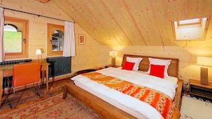 A bedroom with a sloped ceiling, a bed with white and orange bedding, two bedside lamps, and a window. - Chalet François, (Champery). by Interhome (Champery)