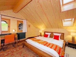 Ein Schlafzimmer mit schrägverdeckter Decke, einem Bett mit weißer und orangefarbener Bettwäsche, zwei Nachttischlampen und einem Fenster.