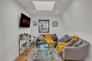 Ein modernes Wohnzimmer mit Flachbildfernseher, einer Couch, einem Couchtisch und einem Fenster mit Blick.