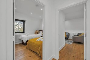 Un dormitorio con dos camas, una ventana, un radiador y un sofá gris en un interior moderno.