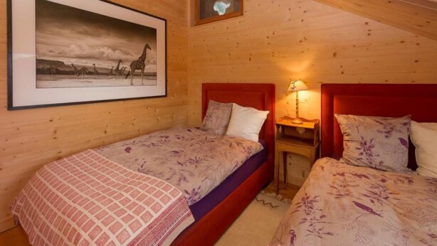 A wooden cabin bedroom with two beds, a framed picture on the wall, and a small table with a lamp. - Chalet François, (Champery). by Interhome (Champery)