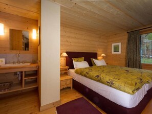 A wooden cabin bedroom with a bed, bedside lamps, a mirror, and a window with curtains. - Chalet François, (Champery). by Interhome (Champery)