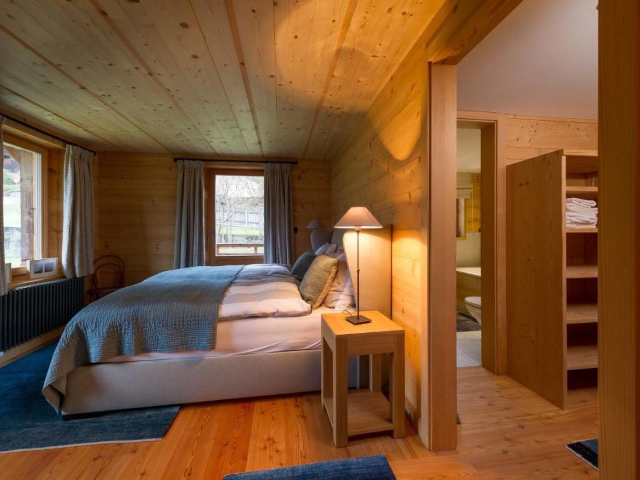 Een slaapkamer in een houten hut met een bed, bedlampje en uitzicht op de omgeving.