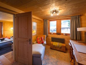 Ein gemütliches Holzhaus-Interieur mit Bett, kleinem Tisch, Heizkörper und einem Fenster mit Vorhängen.