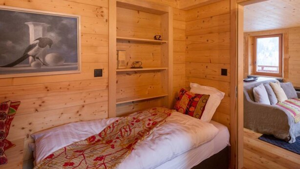 Une pièce dans une cabane en bois, avec un lit, un tableau et une fenêtre.
