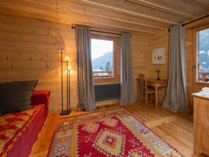 Ein Zimmer in einer Holzhütte mit einem Bett, einem Schreibtisch und Blick auf Berge durch ein Fenster.