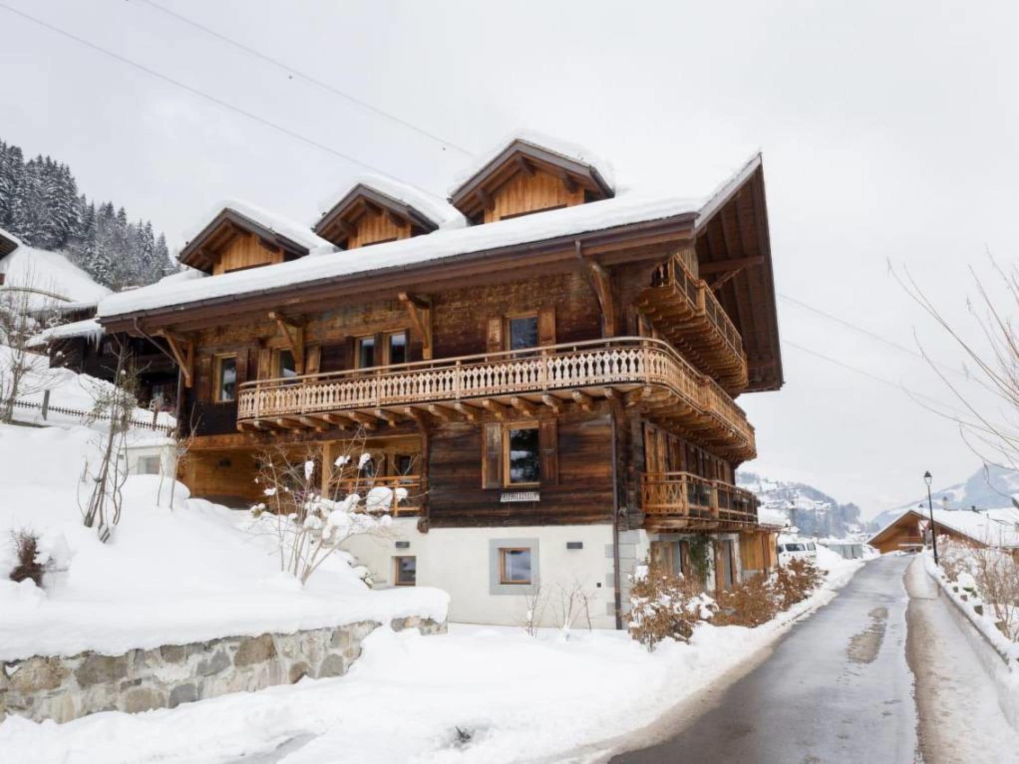 A wooden chalet with a balcony, surrounded by snow-covered ground and mountains.