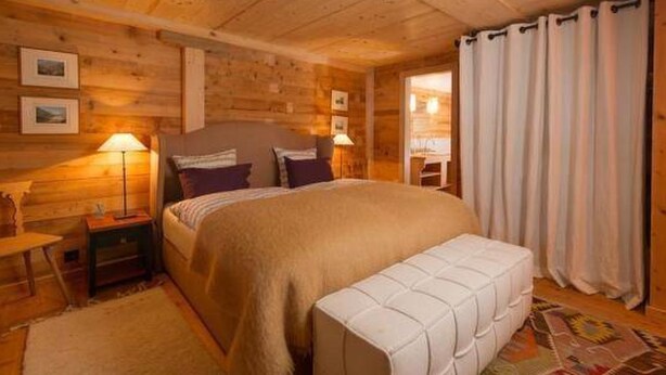 Ein Schlafzimmer einer Holzhütte mit Bett, Nachttischlampen, einer Bank und einem gemusterten Teppich.