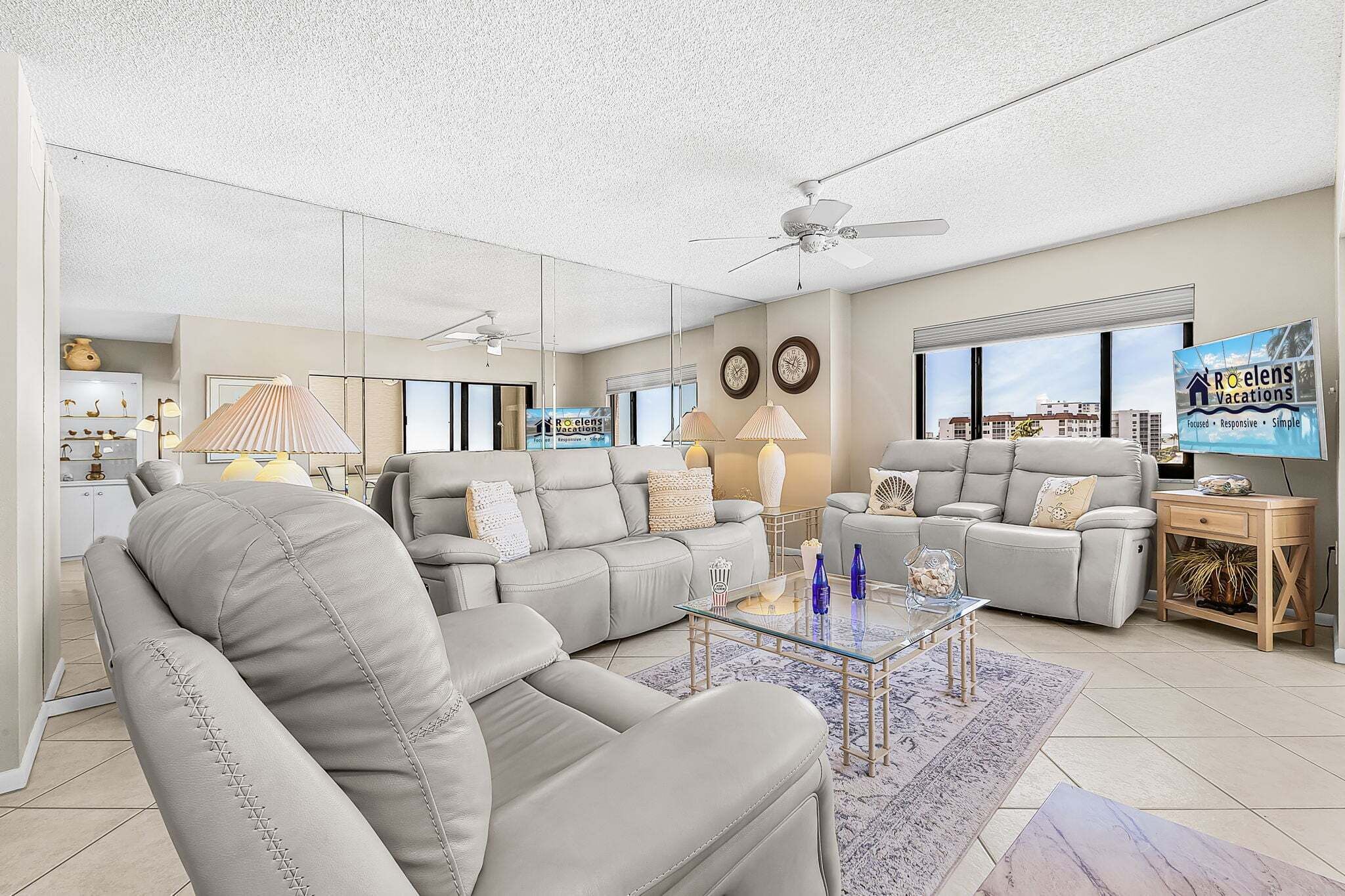 A spacious living room with a sectional sofa, a glass coffee table, and a ceiling fan.