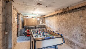 Een kamer met een tafelvoetbaltafel, een bakstenen muur en een plafond met blootliggende leidingen.