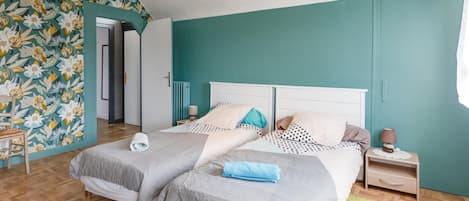 A bedroom with two beds, a wooden floor, a teal accent wall, and a floral wallpaper on one side.