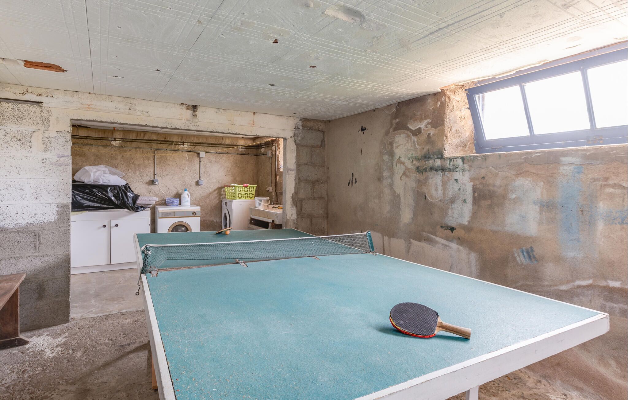 Una habitación con mesa de ping pong, lavadora y ventana.